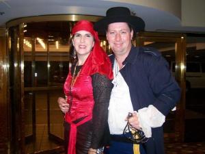 A woman in a red pirate costume and a man in a blue pirate outfit stand together in front of a revolving door, smiling at the camera.