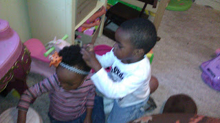 A young boy styling his little sister's hair while she sits patiently.