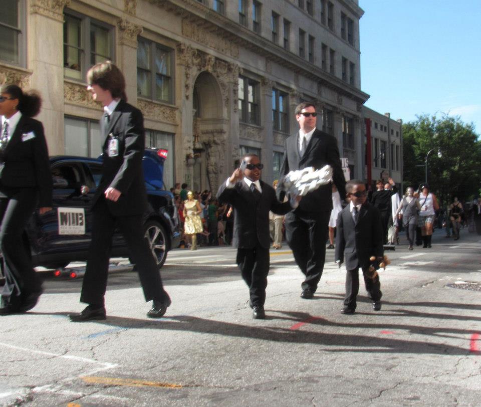 A father and two sons walking in a parade cosplaying as the Men In Black