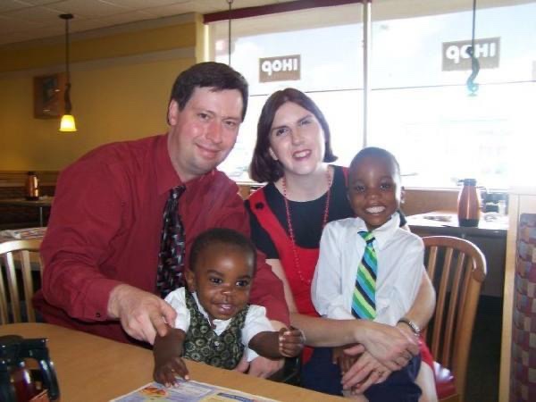 Two white parents smiling with their newly adopted black sons