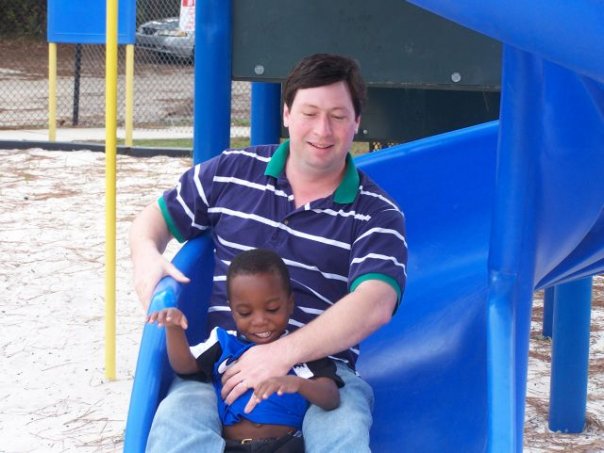 White dad and black child on a slide at the park
